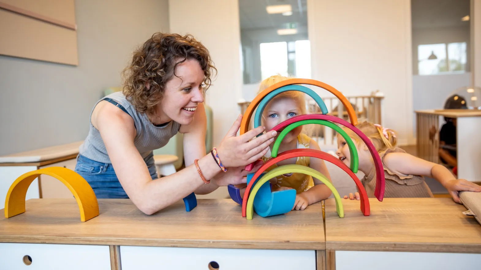 Kind stapelt houten regenboog samen met pedagogisch medewerker bij kinderopvang Kind&co ludens