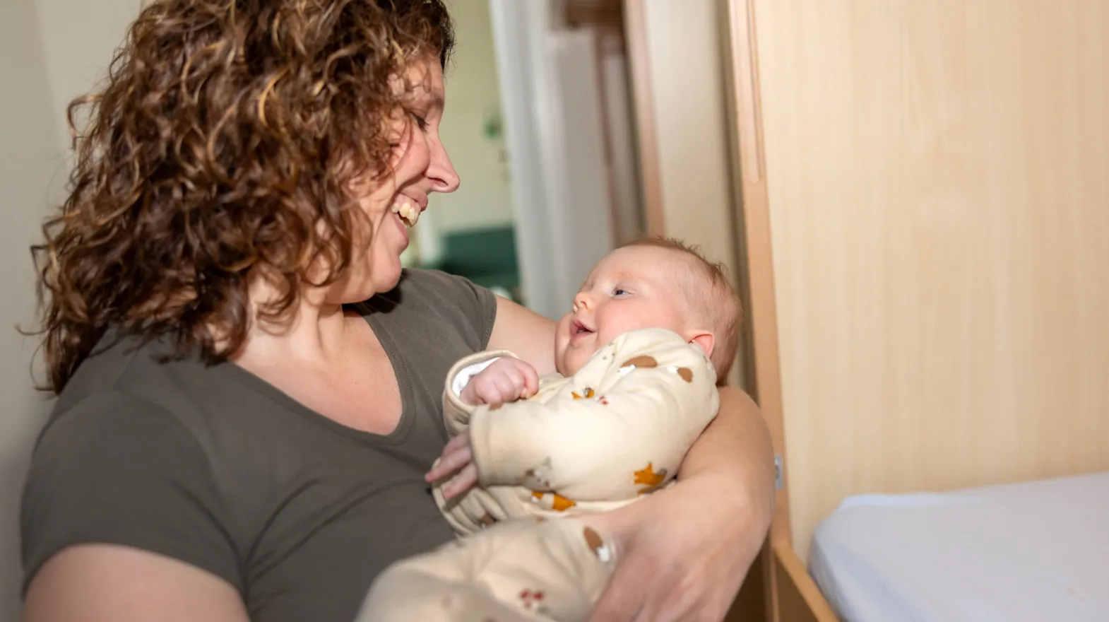 Baby kijkt liefdevol naar pedagogisch medewerker bij kinderopvang Kind&co ludens